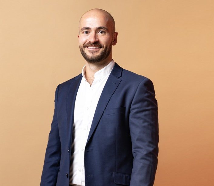 Dr Joep van Agteren, wellbeing scientist, smiling in a navy blazer